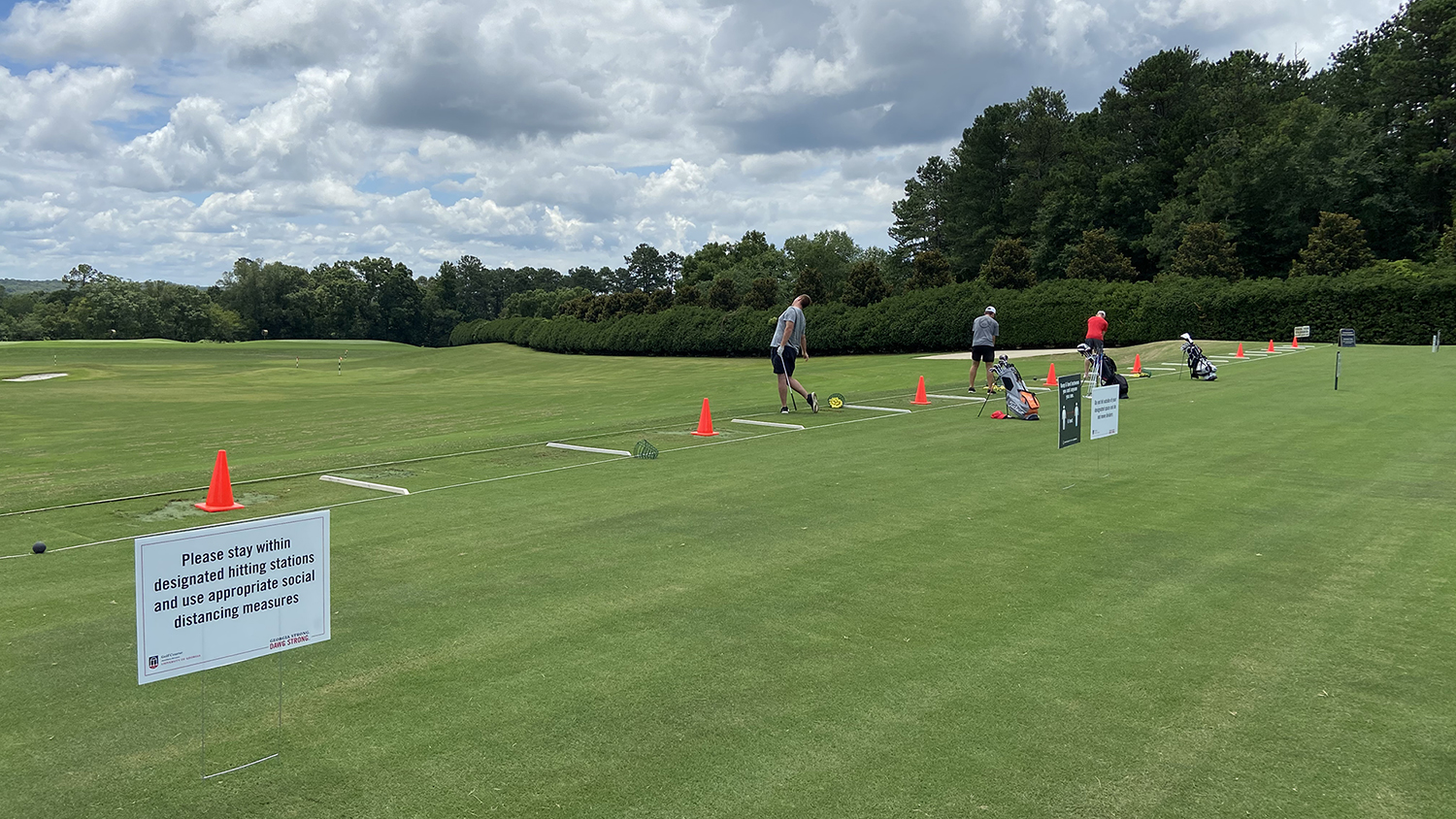 Image of golfers at the driving range, separated into every other station by orange cones. A sign reads "Please stay within designated hitting stations and use appropriate social distancing measures."