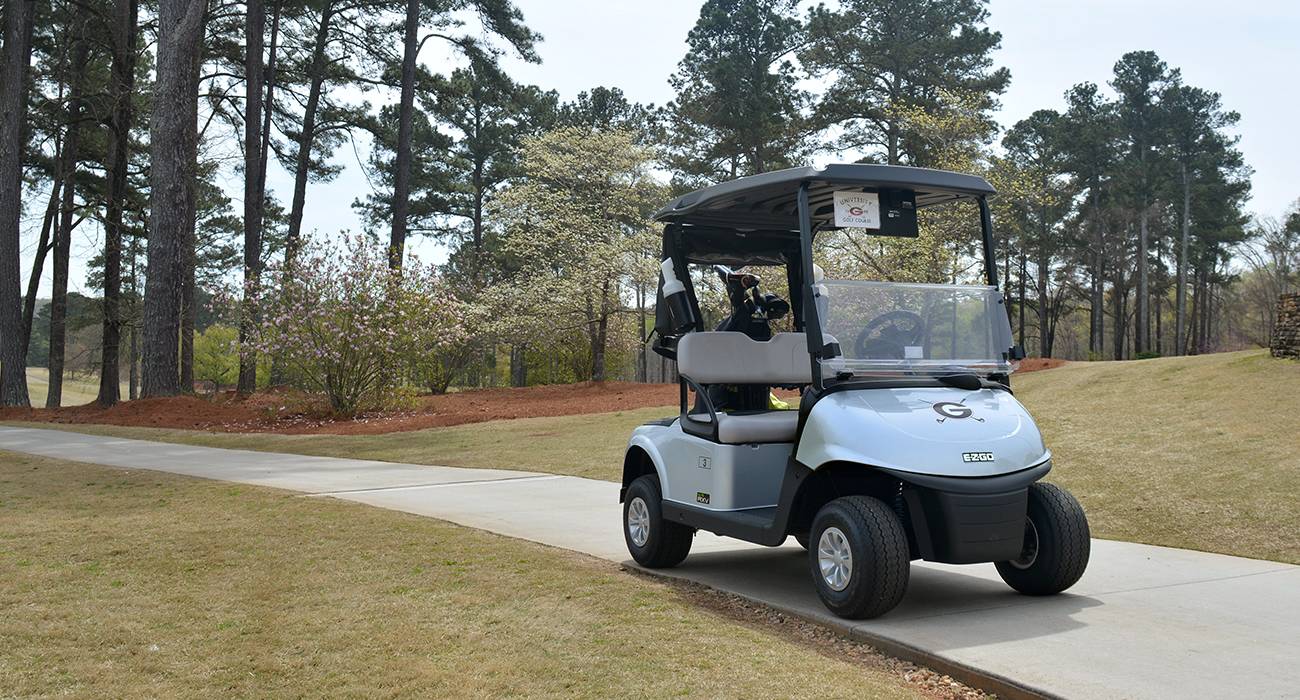 Photo of a golf cart on a path on the course with the UGA Golf Course logo on the front.
