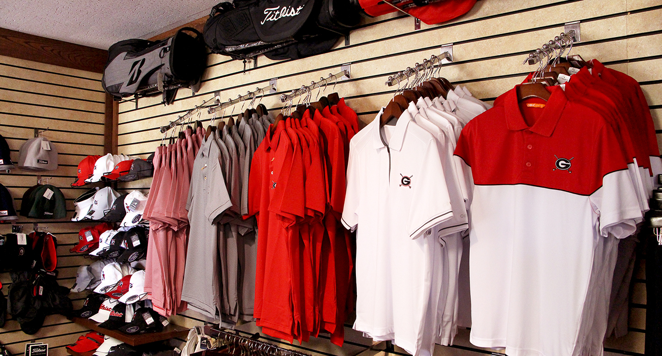 Photo of a display of golf bags and UGA Golf Course branded shirts and hats inside of the Golf Shop.