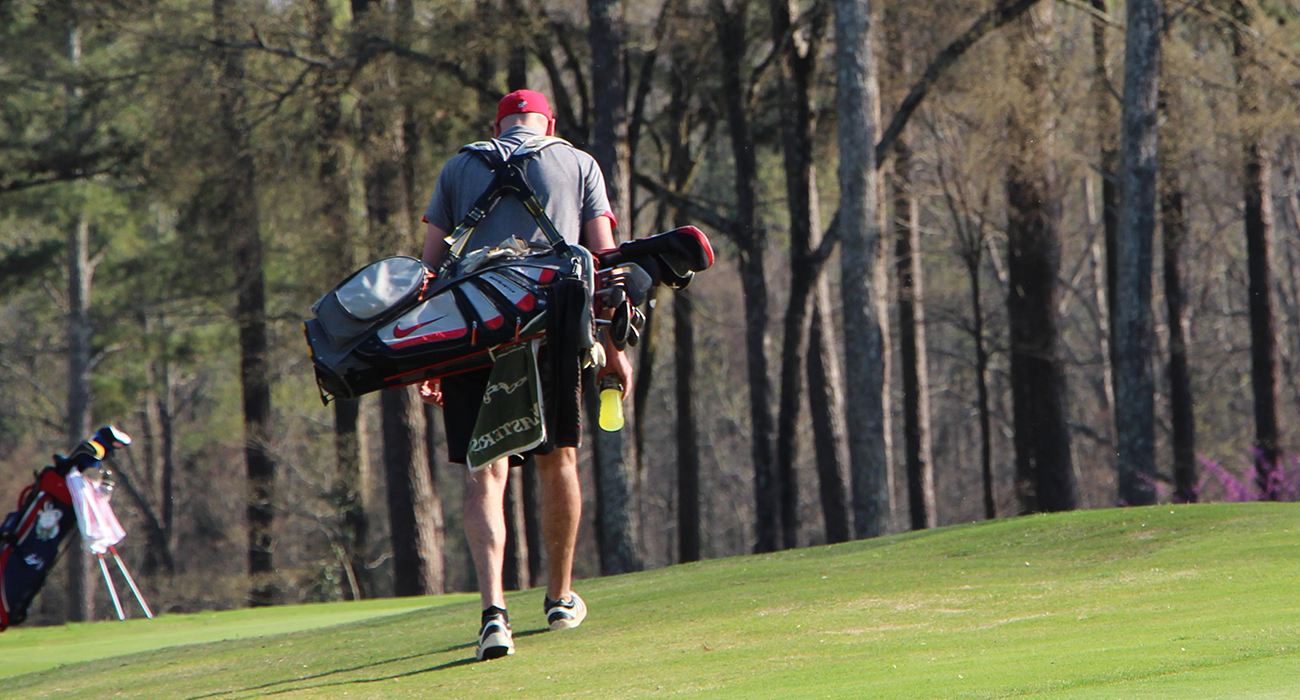 Man walks on the course with a golf bag.
