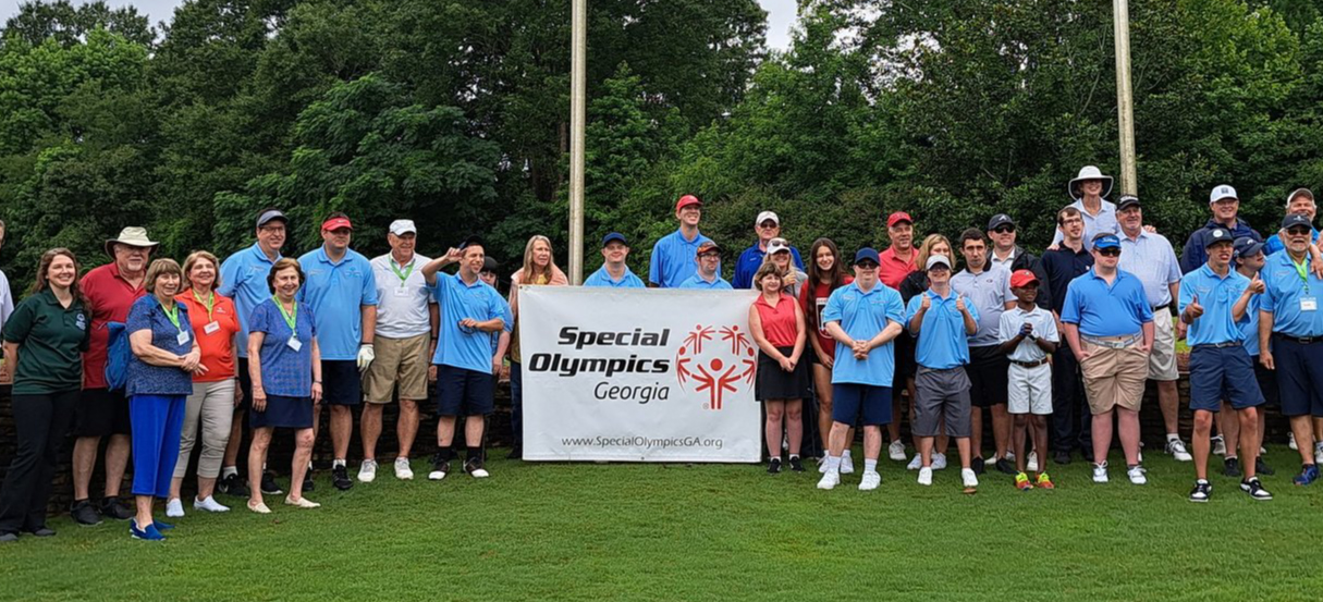 A photograph of a large group of golfers standing on the UGA Golf Course green holding a sign that reads, "Special Olympics Georgia; www.SpecialOlympicsGA.org"
