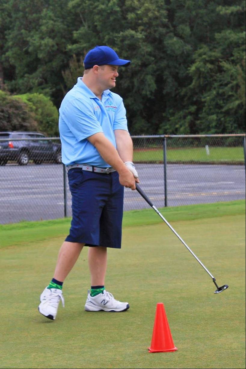 A photograph of a golfer wearing a blue hat and blue shirt, holding a club as if preparing for a swing.